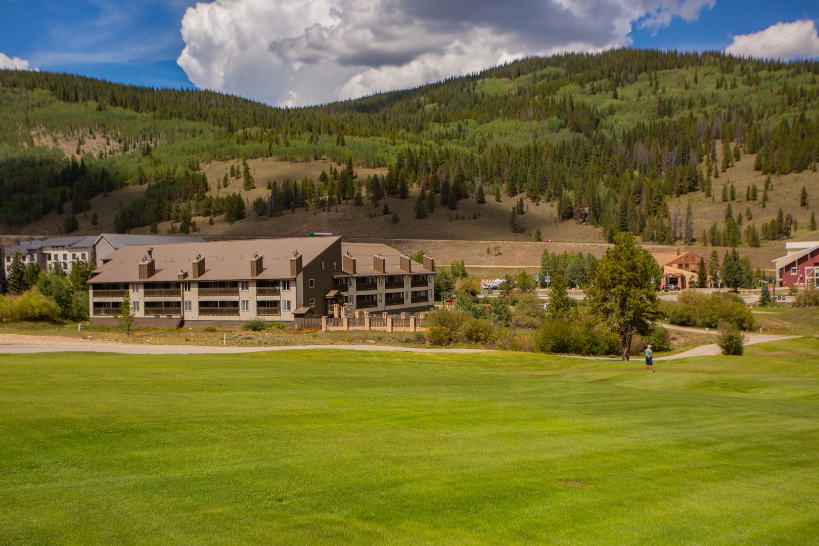 Multi-level vacation rental property nestled in a lush forested valley with manicured green fairways and mountain surroundings captured during a bright summer day.
