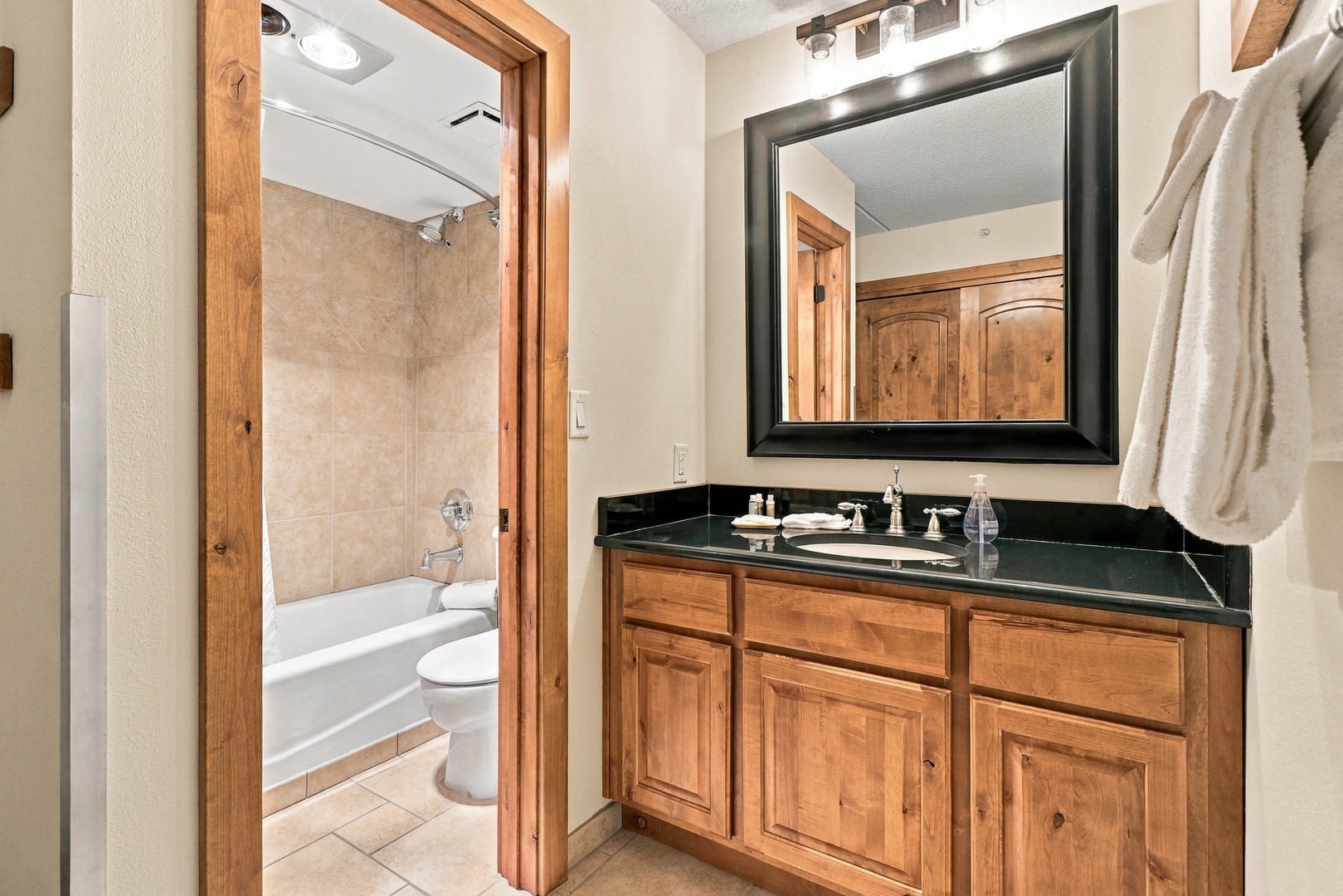 Your bathroom features a sleek vanity with a striking black granite countertop and warm wooden cabinetry. Fresh towels are ready, and a full tub-shower combo awaits just beyond the threshold.