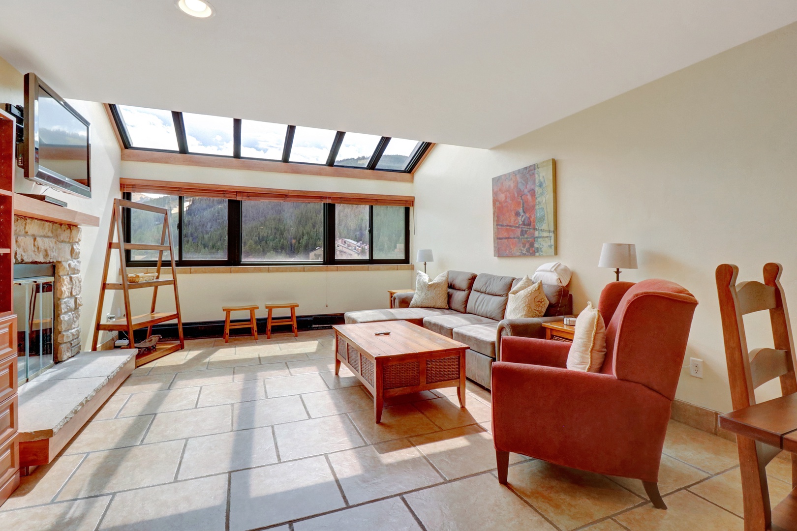 Bright and welcoming living area featuring expansive skylight windows that showcase panoramic mountain views. Comfortable seating and rustic wood accents create a cozy alpine retreat.