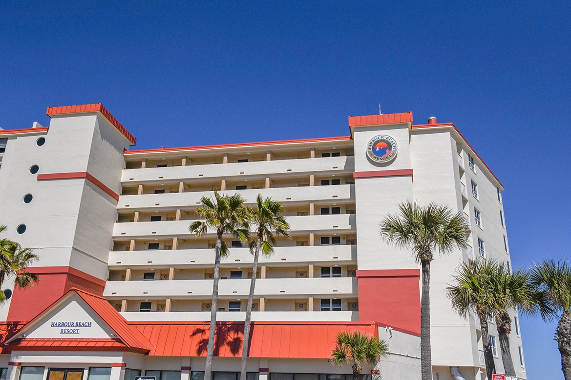 Bright beachfront resort building with vibrant red accents and swaying palm trees under clear blue skies.