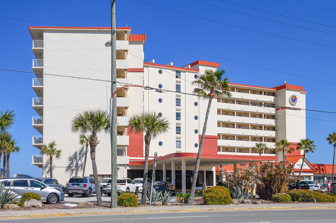 Beachfront hotel with tropical palm trees and convenient parking, featuring white and coral exterior under clear blue skies.