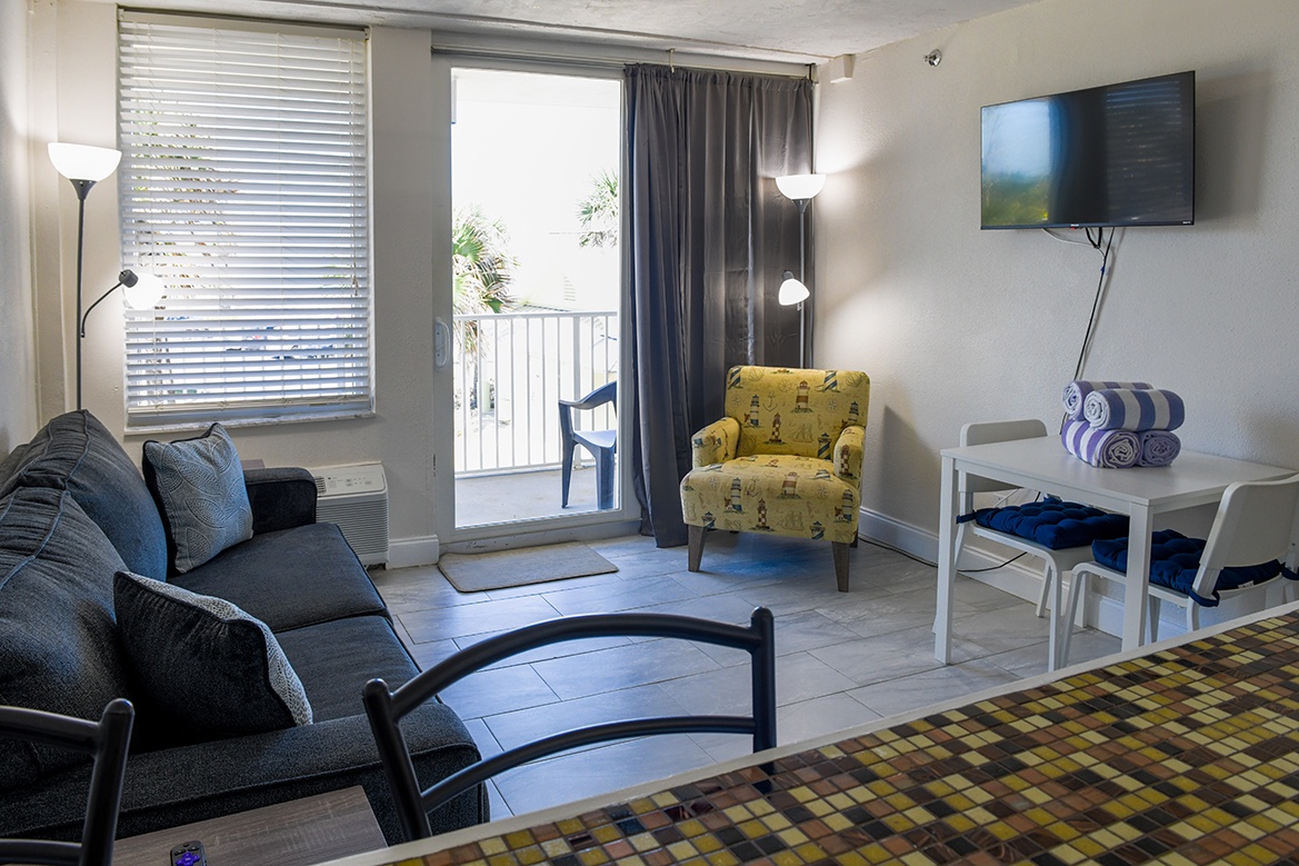 Relax in your bright living space with plush seating, modern TV, and coastal charm through sunny windows.