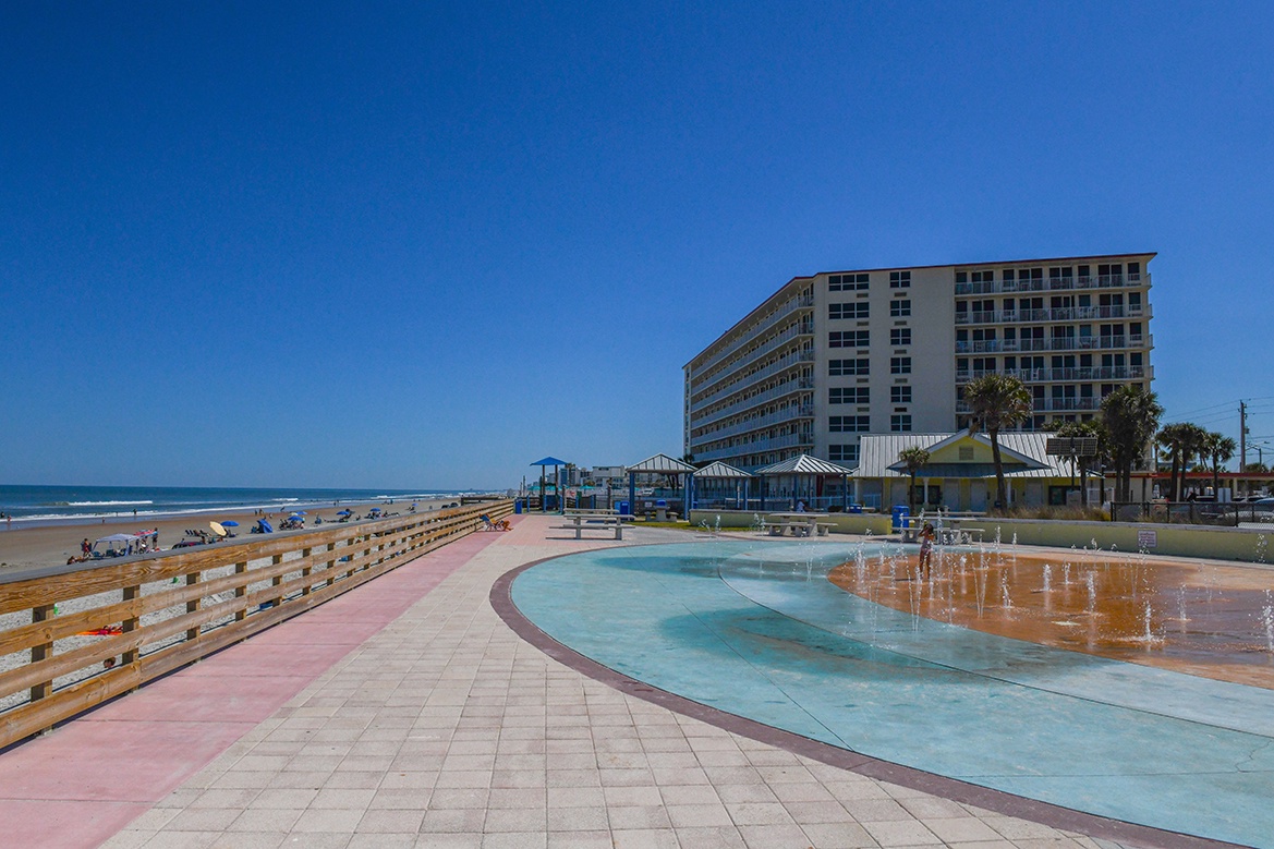 Beachfront property featuring a nearby curved fountain pool and direct sandy beach access under brilliant blue skies.