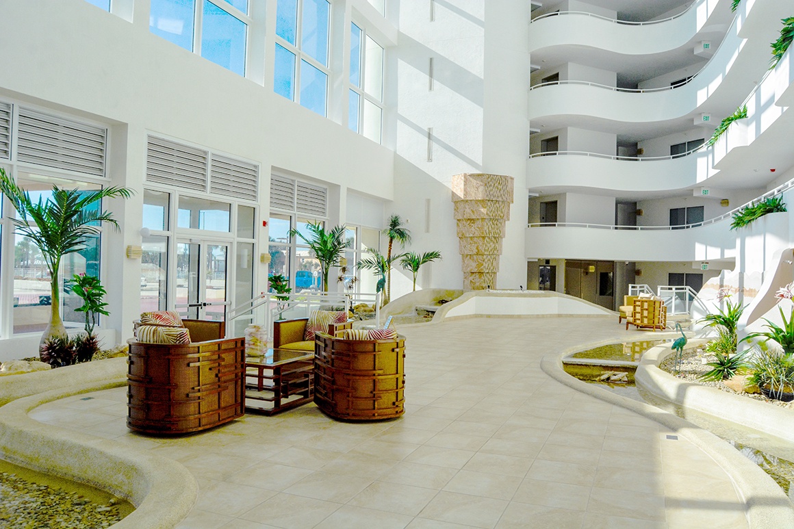 Step into this stunning hotel atrium where modern elegance meets tropical comfort, featuring curved balconies and lush greenery throughout the space.