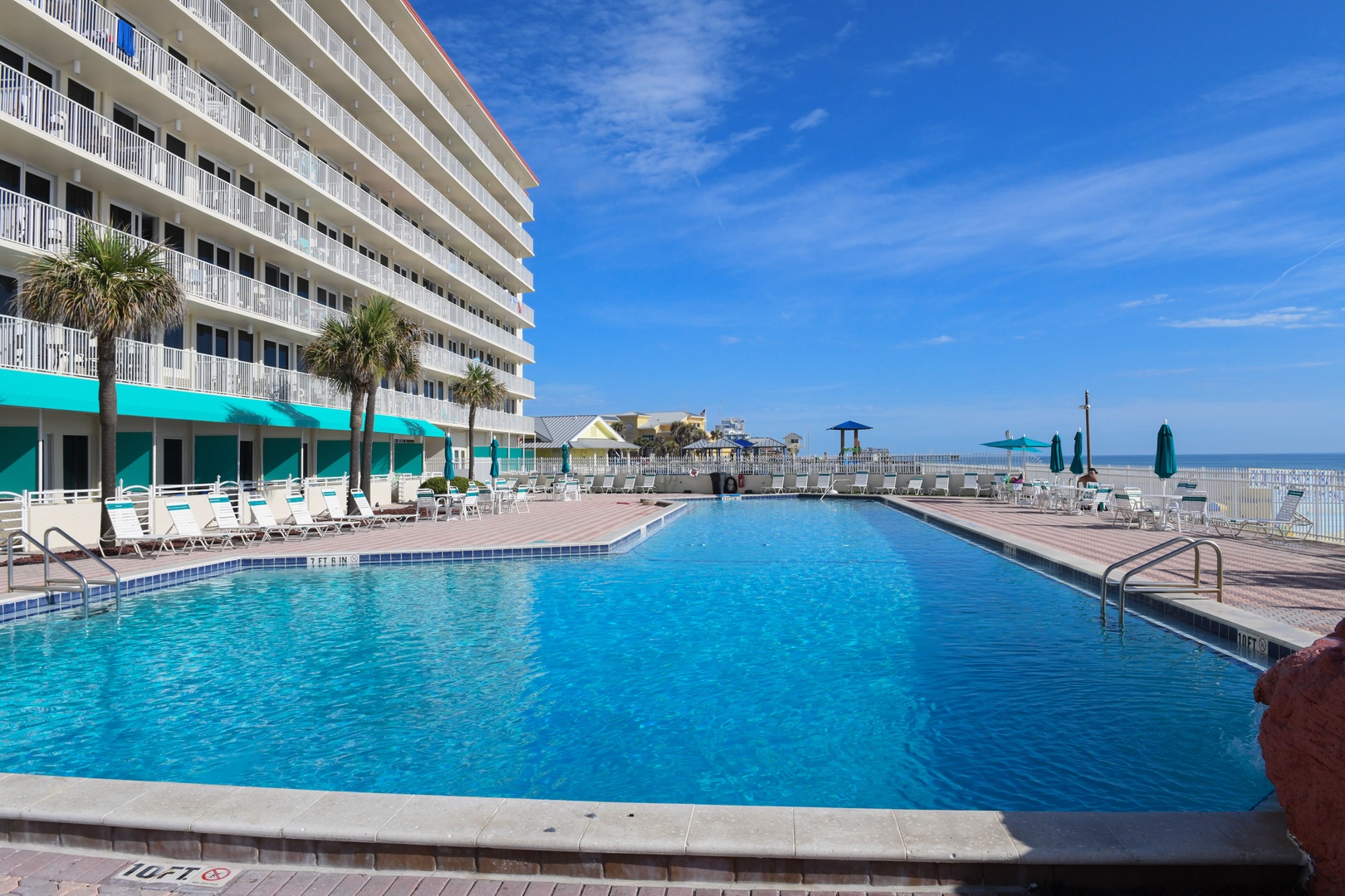 Picture yourself lounging by this sparkling beachfront pool, where turquoise awnings frame your ocean view and gentle palms sway overhead, steps from the pristine Gulf shore.