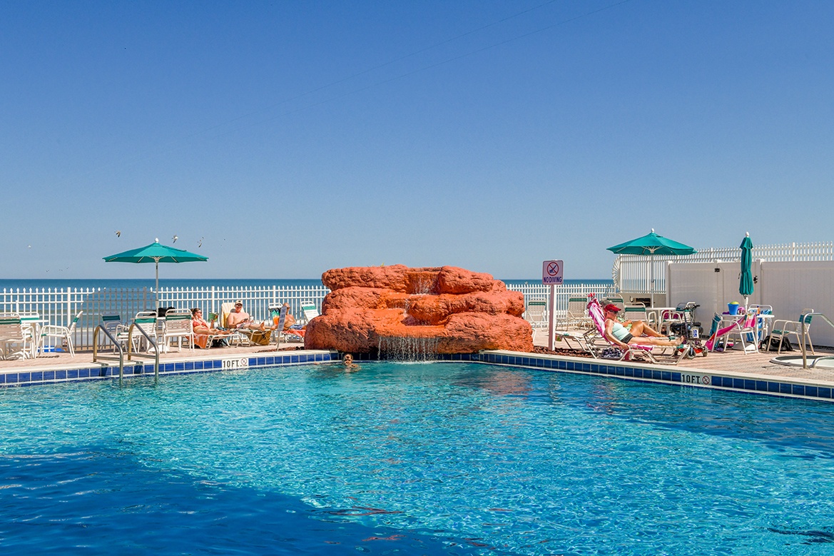 Sparkling pool with decorative rock waterfall creates your perfect poolside retreat under the bright blue sky.
