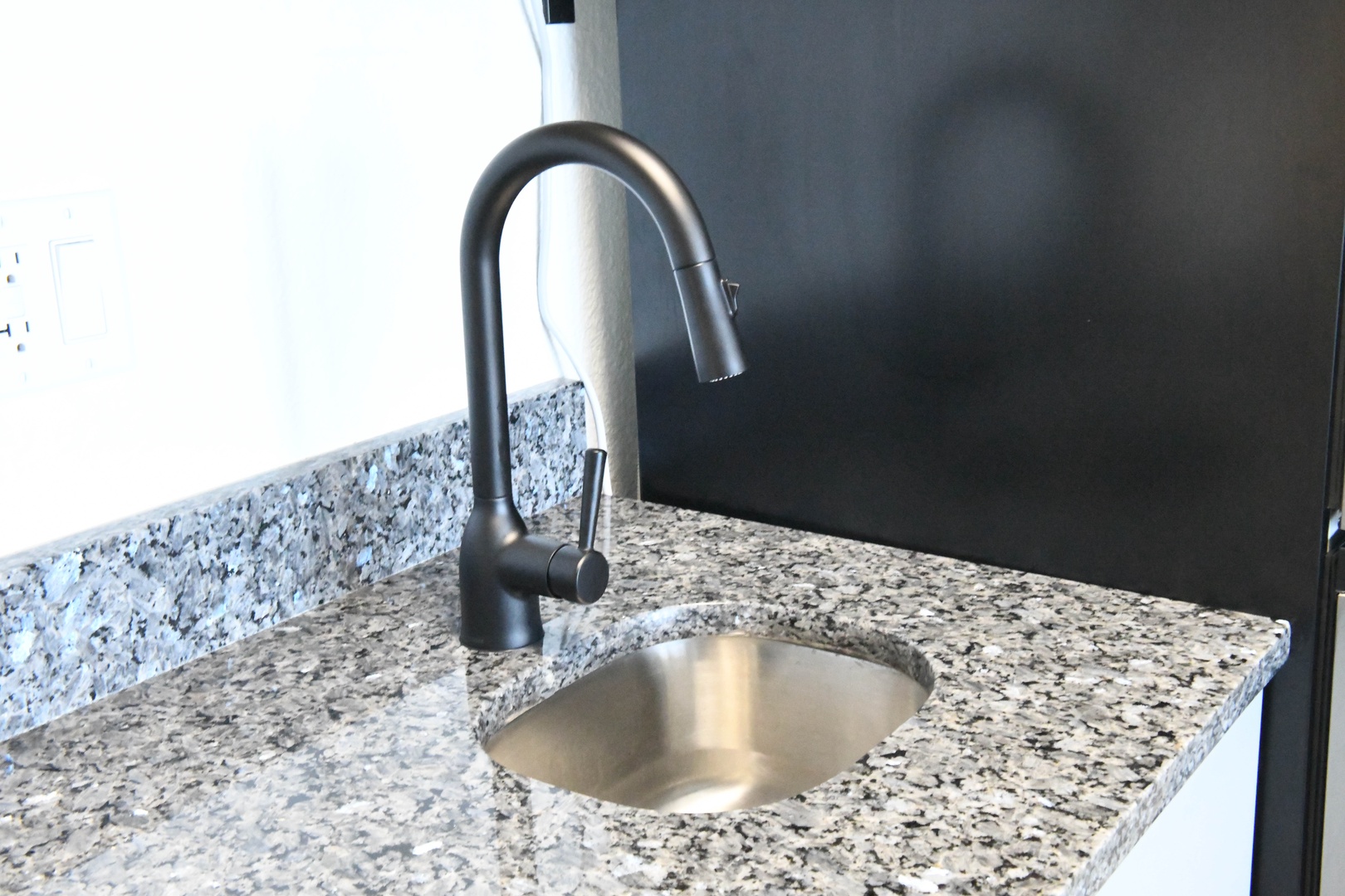 Modern kitchen equipped with a sleek granite countertop, stainless steel sink, and stylish pull-down faucet ready for your meal prep and cooking needs.