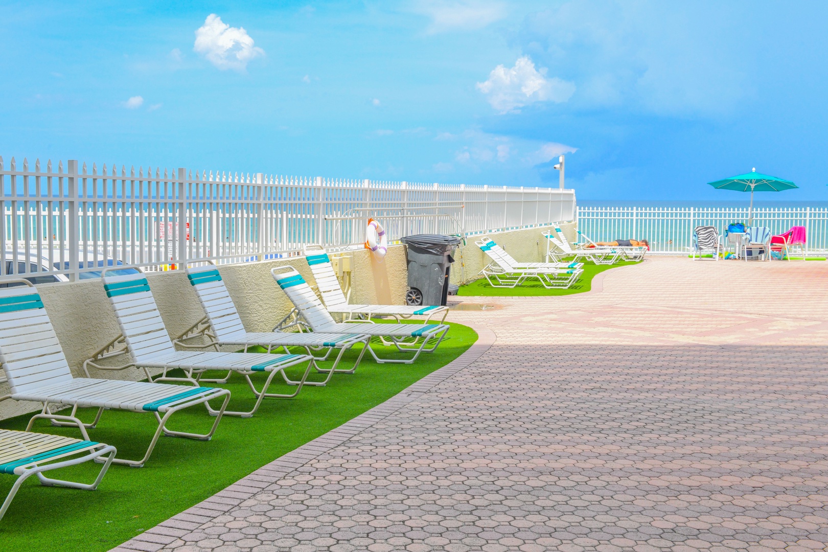 Oceanfront lounging area with colorful beach chairs, lush green turf, and direct access to pristine turquoise waters—ideal for sun-soaked relaxation just steps from the shore.