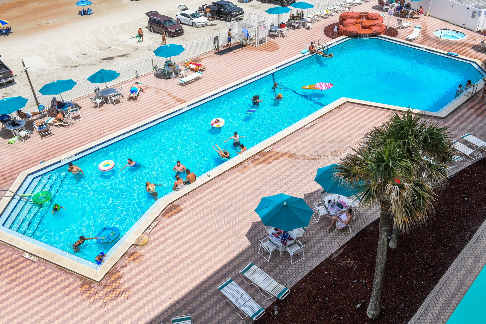 Aerial view of the property's expansive pool area, featuring a large swimming pool with water slide, surrounding deck seating, and beachside access for guests to enjoy.