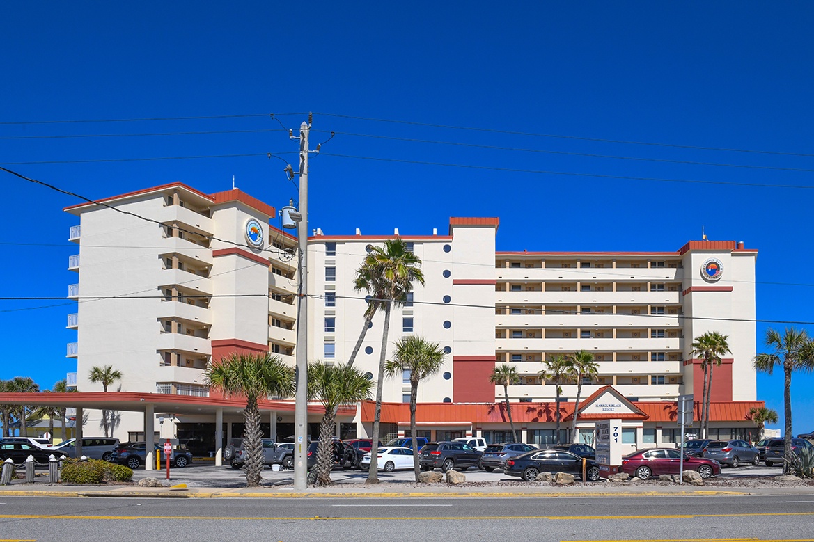 Multi-story beachfront hotel with tropical palms and convenient parking, located on a main road for easy access to local attractions.