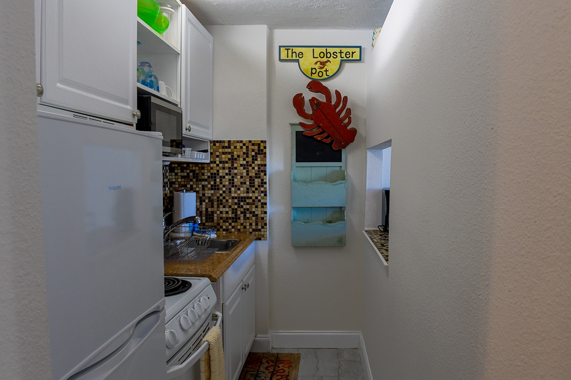 Your galley kitchen features white appliances, mosaic backsplash, and charming coastal touches that make meal prep feel like seaside living.