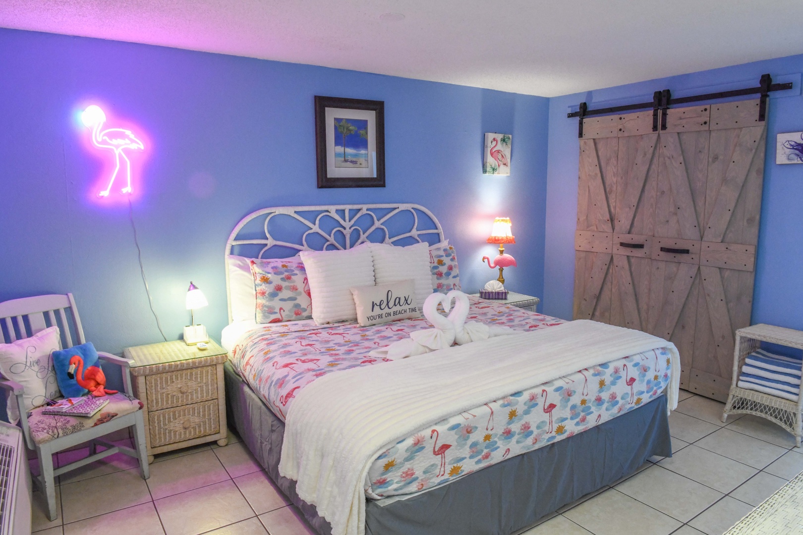 Your cheerful flamingo-themed bedroom features a plush bed dressed in tropical linens, a glowing neon flamingo accent, and rustic barn doors that invite relaxation and fun.