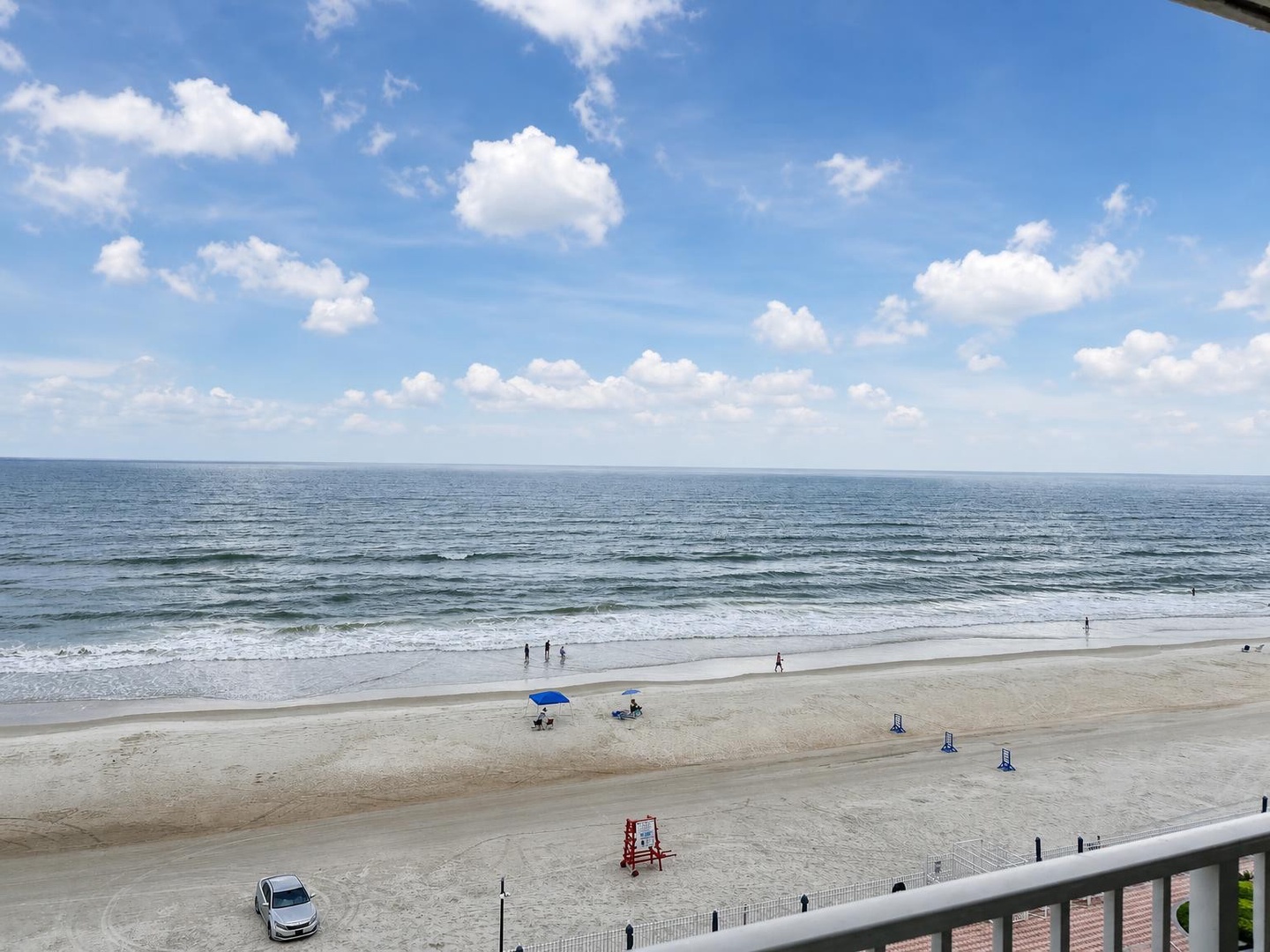 A peaceful stretch of sandy shoreline meets gentle waves under a bright, cloud-dotted sky. The property offers direct beach access with unobstructed ocean views from your balcony.