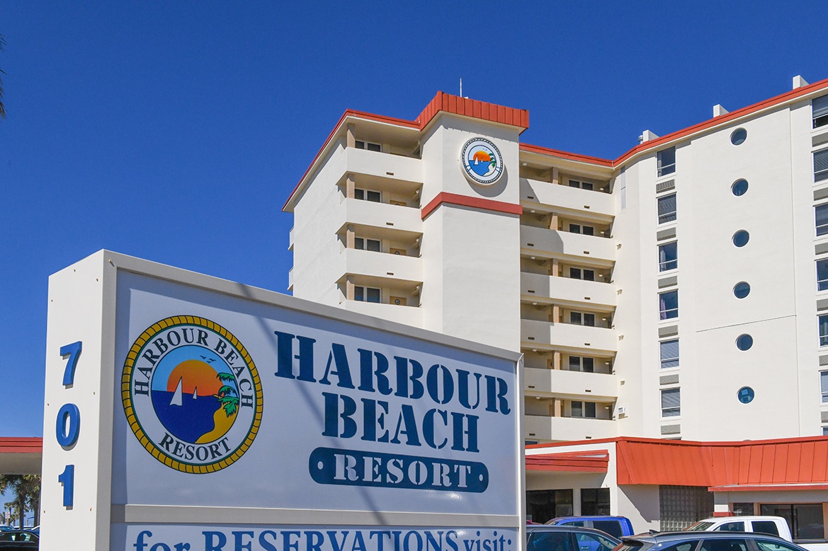 Harbour Beach Resort stands ready to welcome guests with its distinctive white and coral facade under bright blue skies.