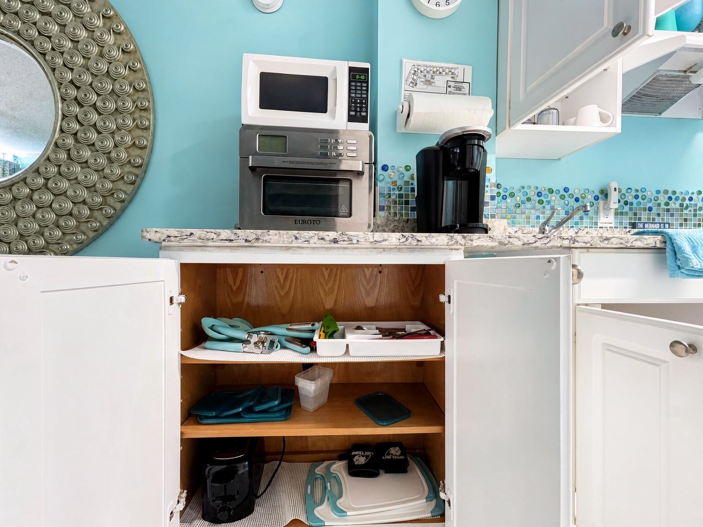 Your fully equipped kitchenette features everything you need—microwave, toaster oven, coffee maker, and thoughtfully organized storage with fresh turquoise accents throughout.
