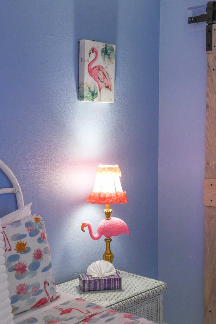 Whimsical flamingo art and a charming lamp bring playful tropical flair to your bedroom corner.
