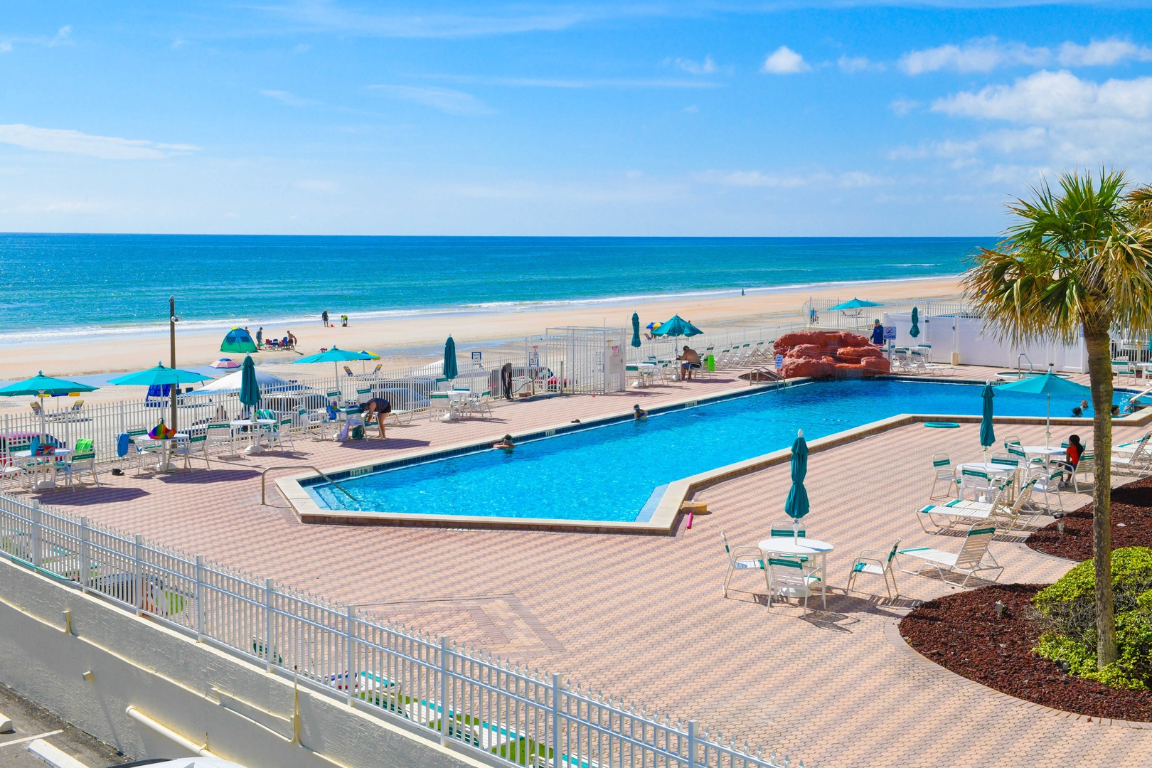 The sparkling pool meets pristine beachfront, surrounded by turquoise waters and soft sands, creating an inviting coastal oasis perfect for sun-soaked relaxation.