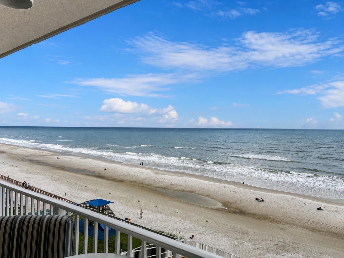 Expansive sandy shores meet gentle waves beneath a bright blue sky dotted with clouds, creating a serene coastal setting ideal for beachside relaxation.