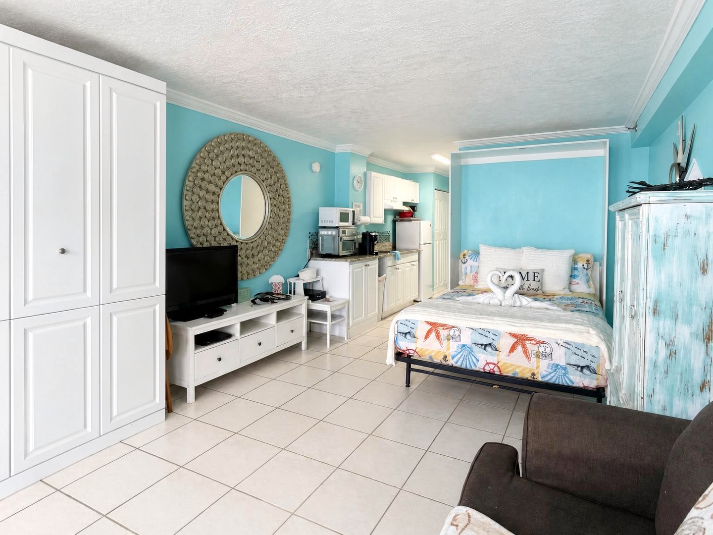 Your bright coastal retreat features a cozy bed dressed in beach-inspired linens, a kitchenette for easy meal prep, and cheerful turquoise walls that bring the ocean vibe right inside.