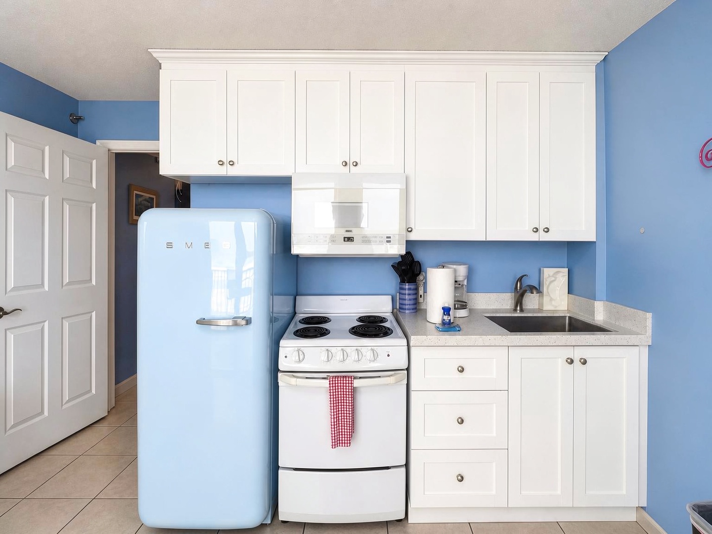 Step into your charming kitchen with crisp white cabinetry and cheerful blue walls. A vintage-style blue refrigerator adds playful character, while your fully equipped cooking space has everything you need to whip up snacks or meals during your stay.