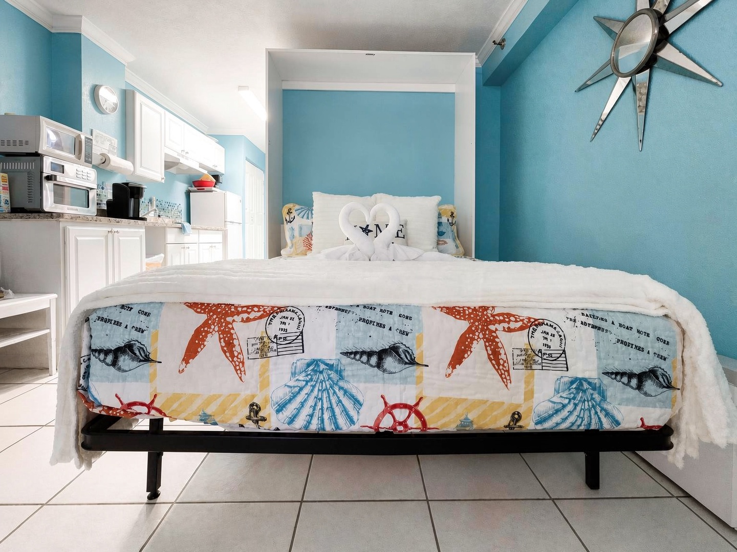 Your cheerful coastal studio brings ocean vibes to life with soothing turquoise walls, beach-themed bedding, and a compact kitchen ready for morning coffee—everything you need for a relaxing seaside escape.