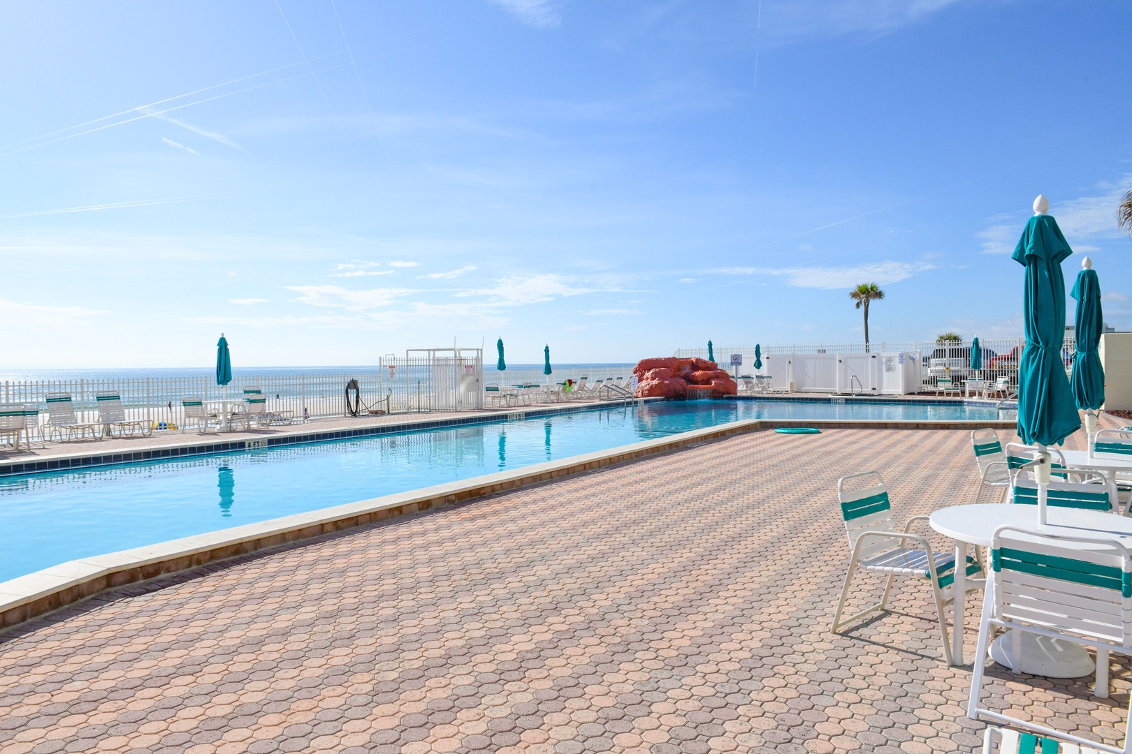 A sparkling pool offers direct ocean access, with lounge chairs and umbrellas perfectly positioned for soaking up the sun and sea breeze under clear blue skies.