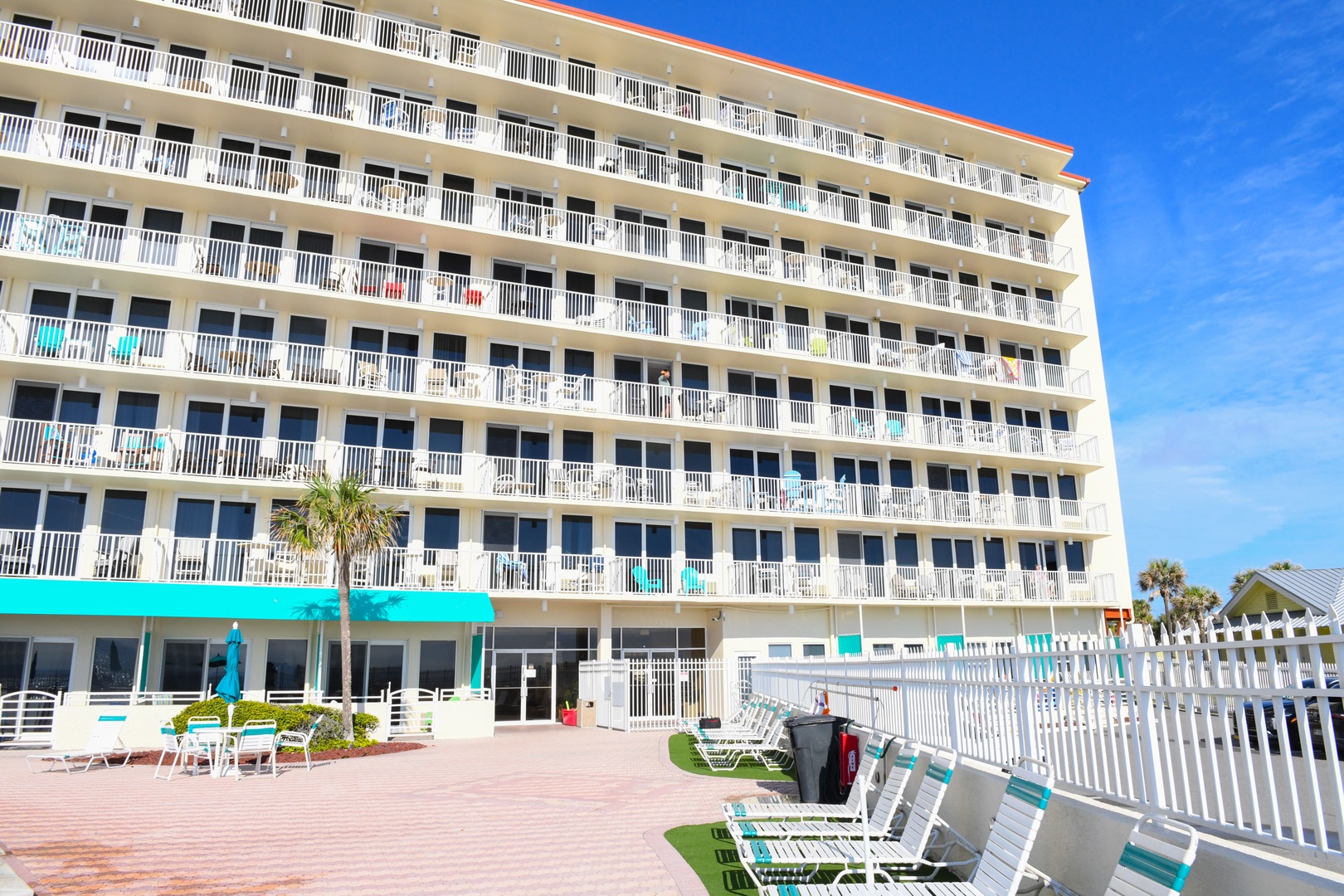 A beachfront property featuring multiple balconies, poolside lounge chairs, and tropical palms, offering direct access to coastal relaxation and sunny Florida charm.