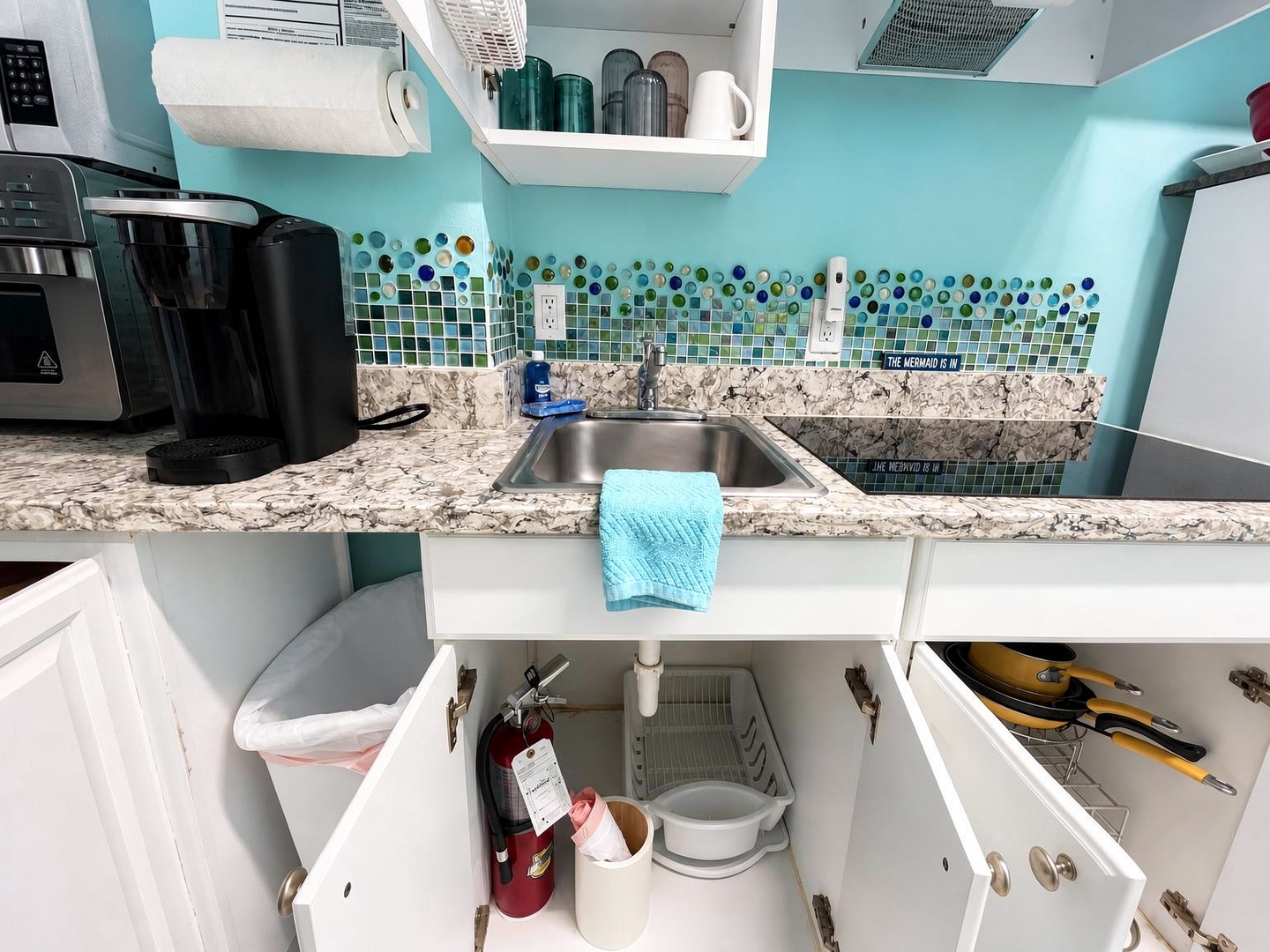Your fully equipped kitchenette features cheerful turquoise walls, granite countertops, and ocean-inspired mosaic tile backsplash—perfect for preparing quick meals or morning coffee in a bright, coastal-inspired space.