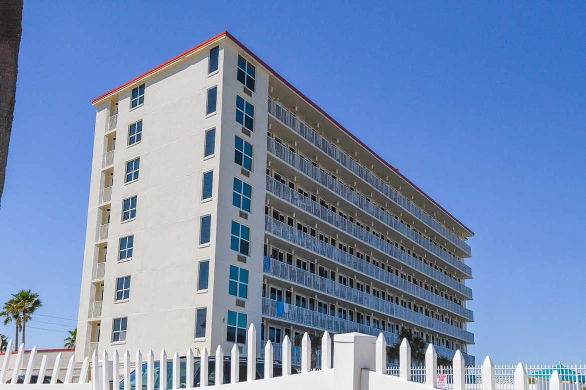 Multi-story beachfront building with private balconies overlooking tropical surroundings under clear blue skies.