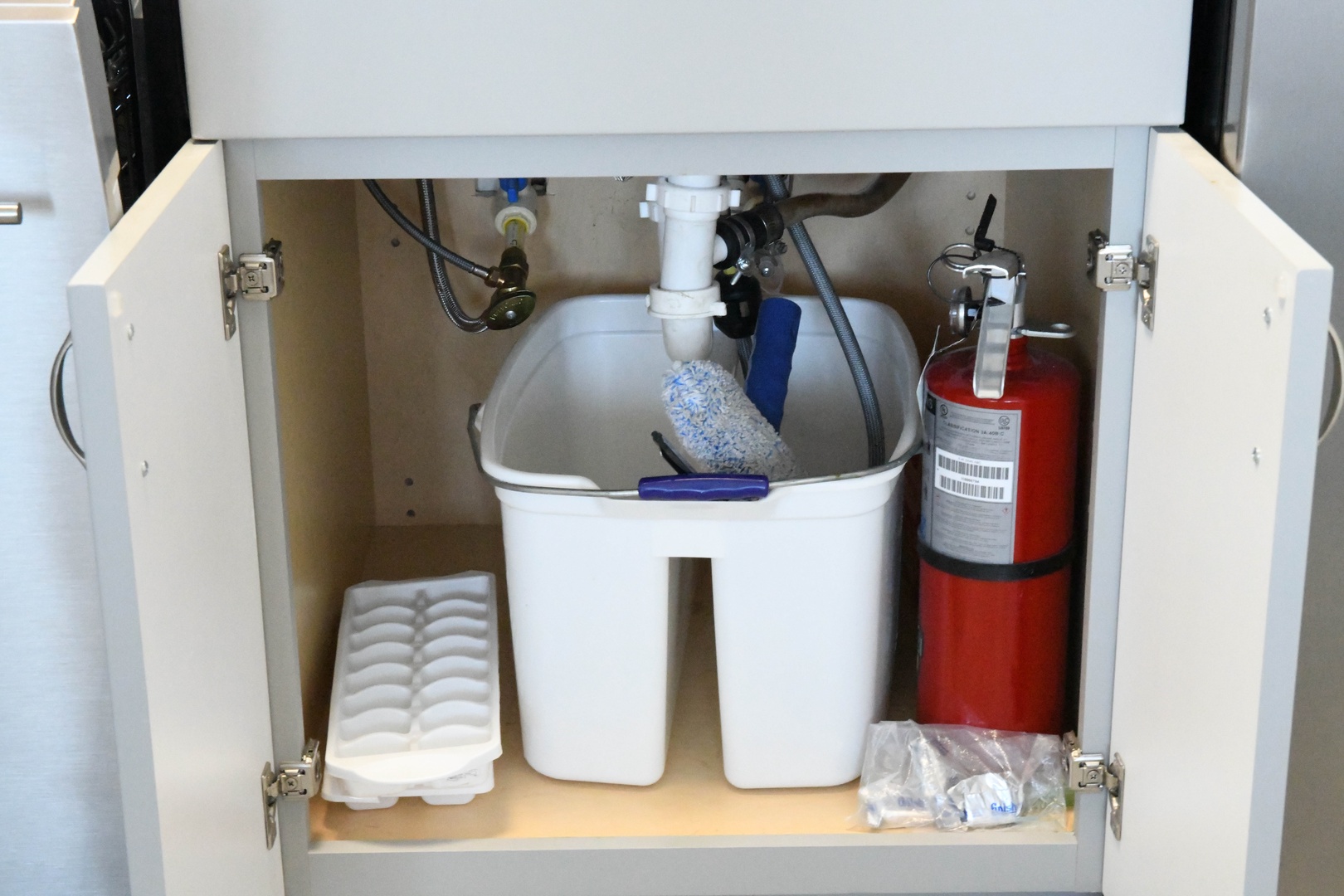 An organized under-sink cabinet with plumbing, a small fire extinguisher, storage containers, and supplies—practical touches ensuring your comfort and safety.