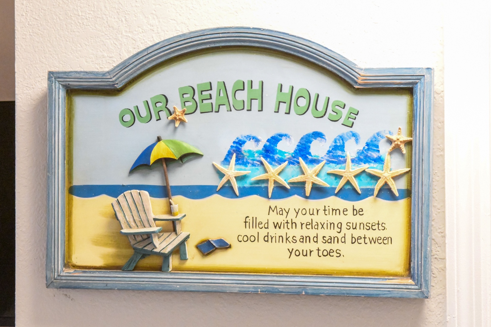 Charming property sign welcomes guests with a beachy message featuring waves, starfish, and a cozy chair by the shore—setting the tone for your coastal getaway.