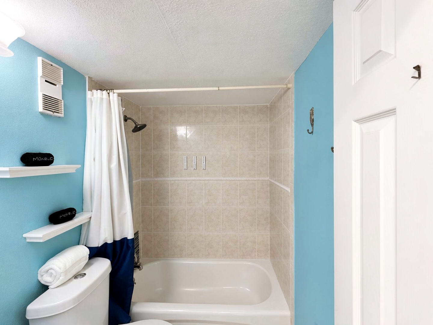 Your private bathroom features a spacious tub-shower combo with crisp white linens, beach-inspired décor, and calming blue accents that set a relaxing coastal tone.