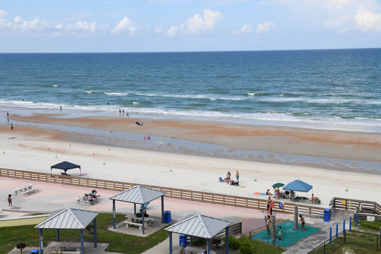 Expansive beachfront area with sandy shores, gentle waves, and recreational facilities including pavilions and a splash pad near the property.