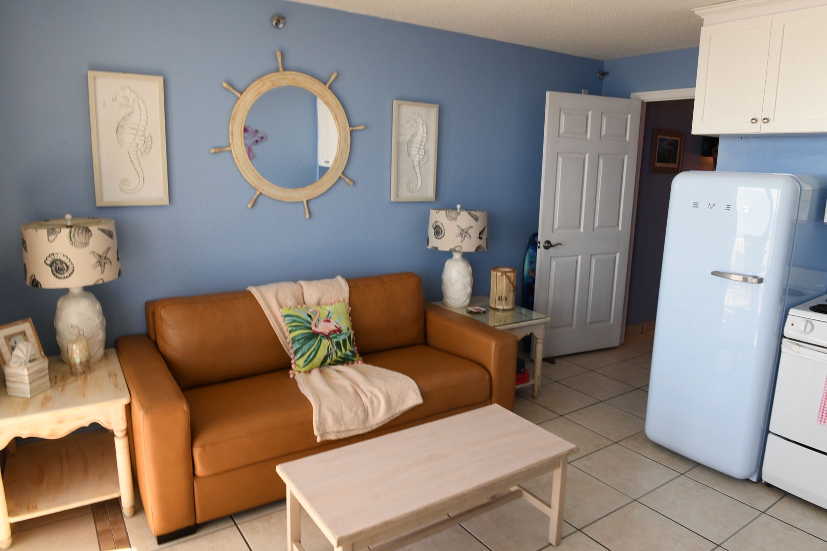 Your coastal retreat features a cozy living space with nautical charm, complete with a comfy sofa and vintage-inspired fridge for storing all your beach day snacks.