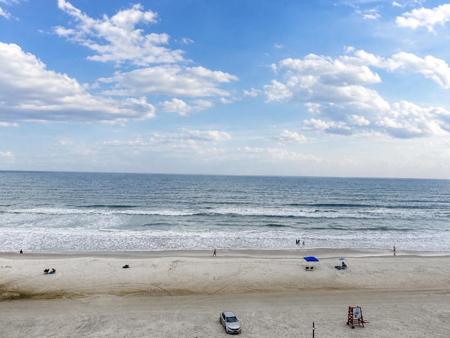 Wide sandy shores meet gently rolling surf beneath a dramatic sky, with ample room for beach strolls and sun-soaked afternoons by the water.