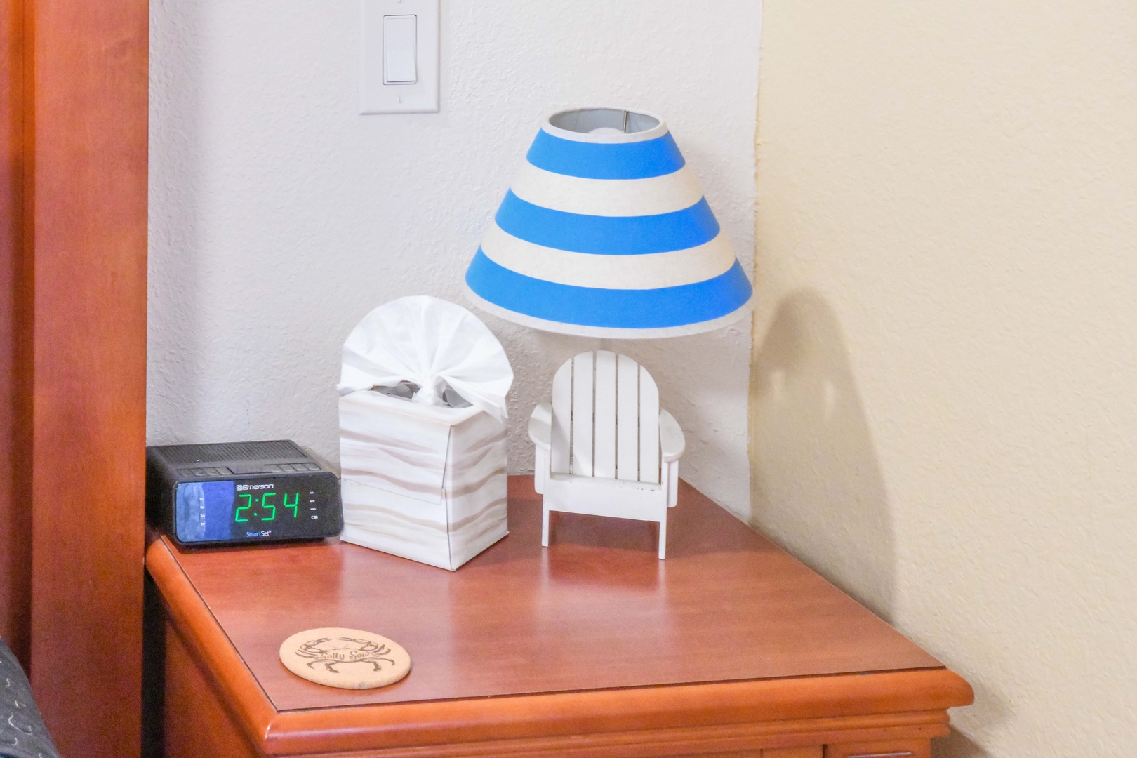 Your cozy bedside setup features a cheerful striped lamp, a tissue box, and a digital alarm clock to help you start each day comfortably.