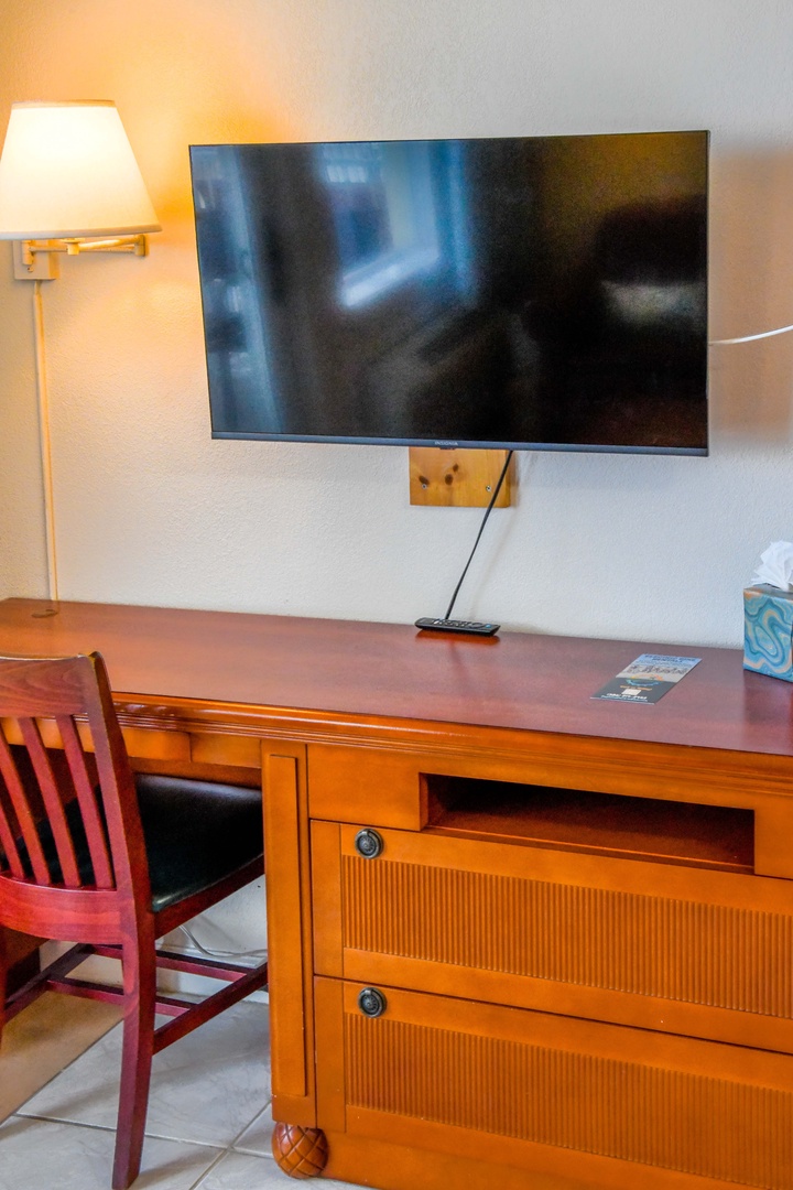 Unwind in your thoughtfully designed workspace featuring a flat-screen TV, warm lighting, and a handcrafted wooden desk perfect for catching up on work or relaxing.