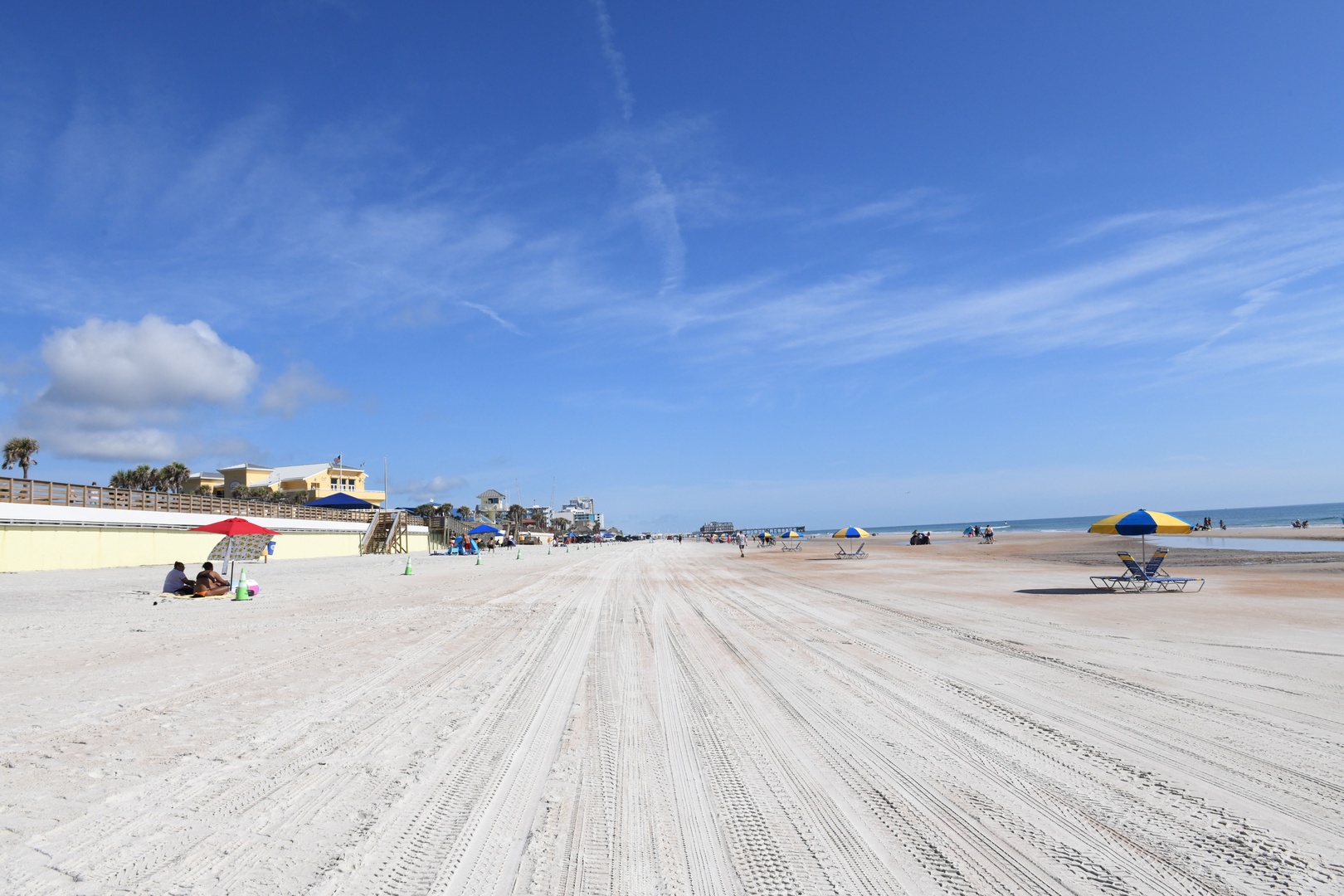 Wide, sandy beach with gentle waves and colorful umbrellas dotting the shore, offering plenty of space to relax under blue skies.