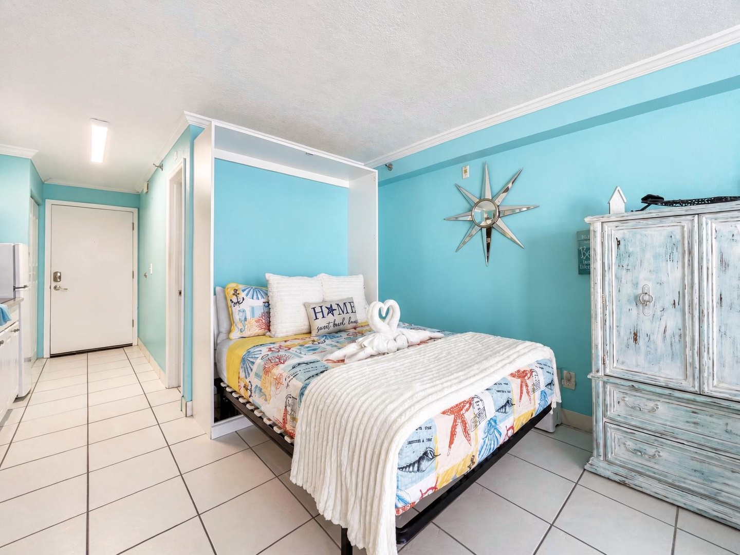 Bright coastal hues wrap around your cheerful sleeping space, where playful beach-themed bedding and a driftwood-style armoire create a relaxed, seaside vibe that invites easy mornings and restful nights.
