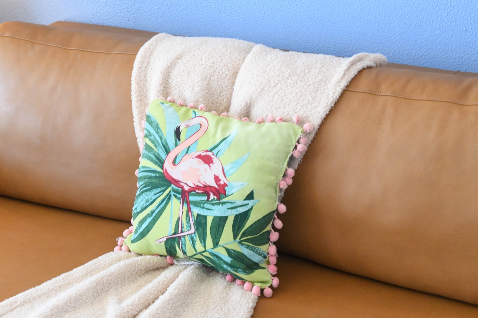 A cozy corner with a playful flamingo pillow and plush throw draped over soft leather seating—perfect for curling up and unwinding.