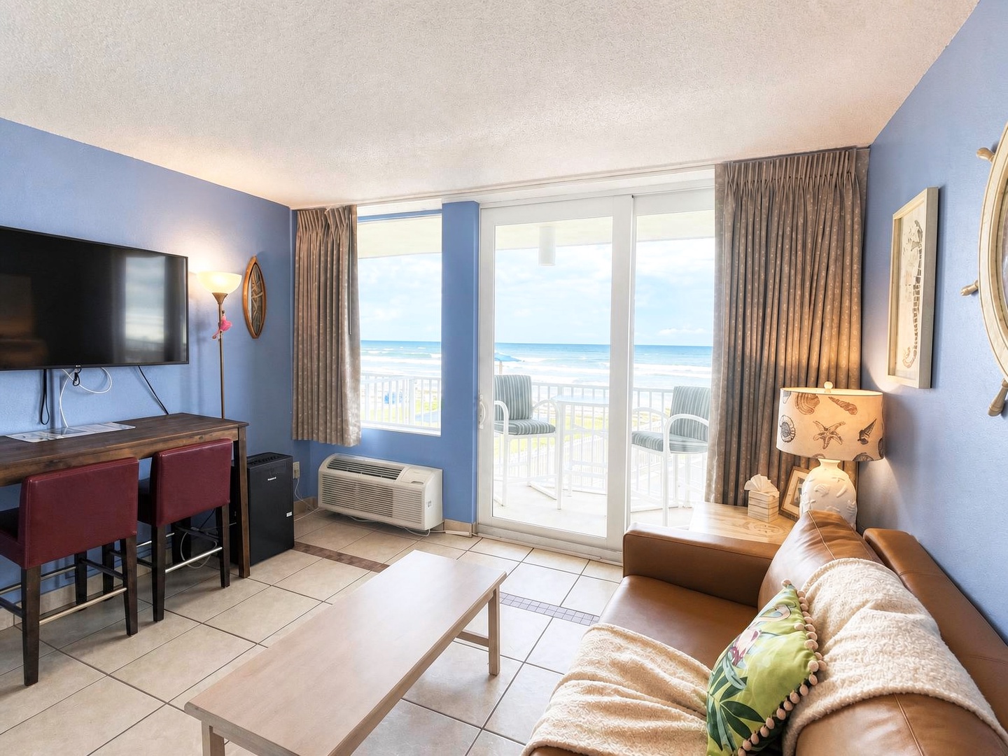 Step into your coastal retreat where ocean breezes and stunning views greet you through expansive balcony doors. Relax on comfortable seating as you watch waves roll in, or unwind with your favorite shows after a sun-soaked beach day.