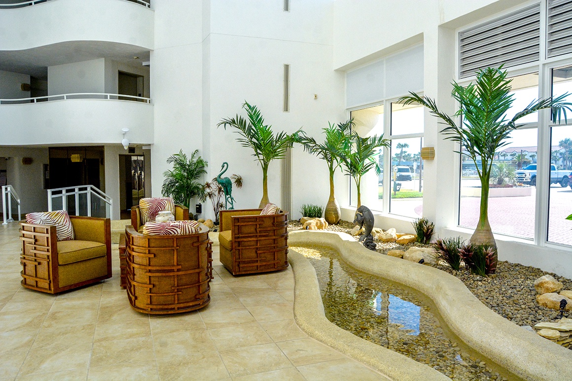Relax in this serene lobby featuring tropical palms and a tranquil water feature, creating your perfect peaceful escape.