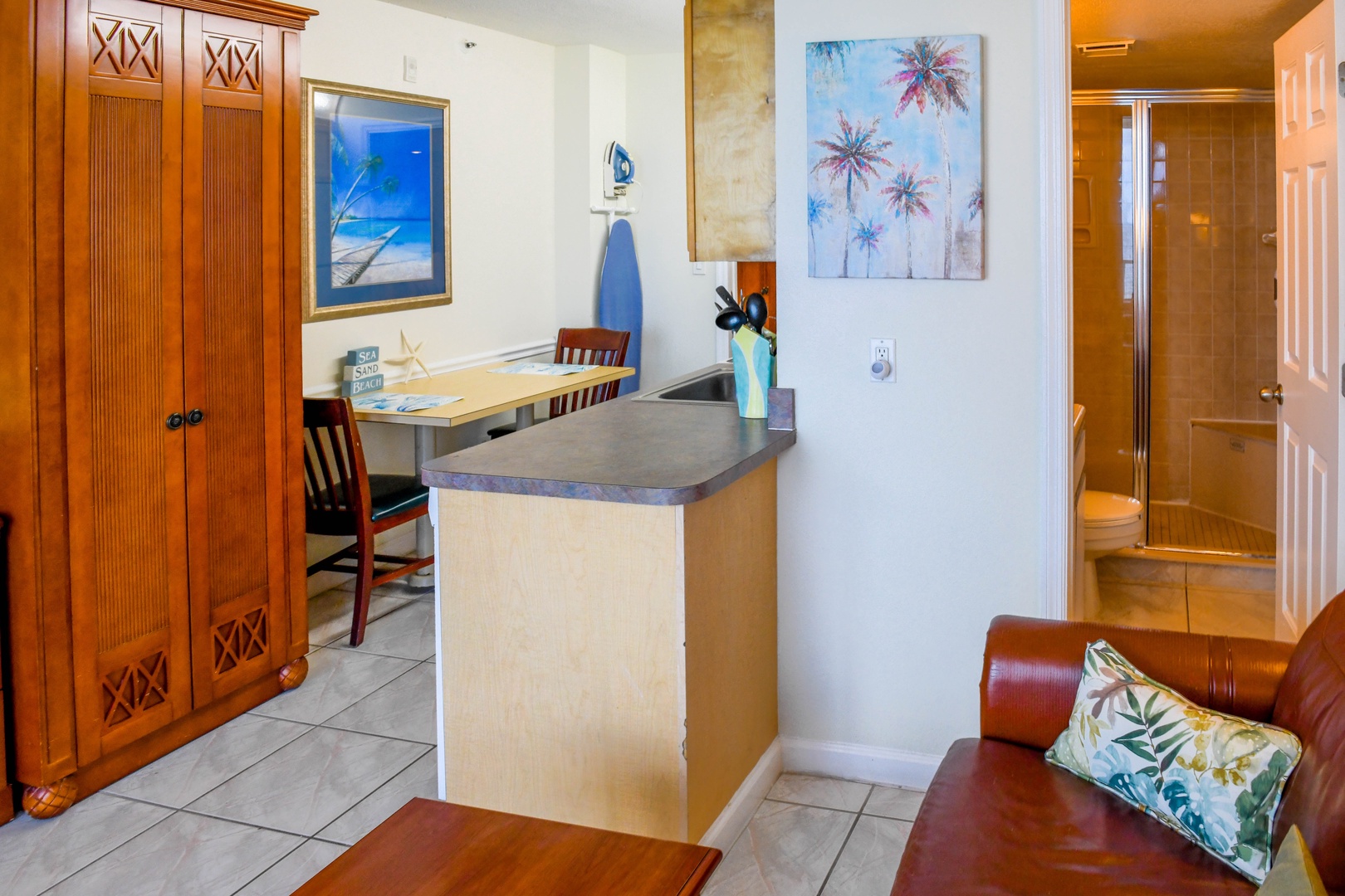 Settle into your spacious open-concept retreat with coastal charm, featuring a fully equipped kitchen, cozy dining nook, and tropical-inspired artwork—perfect for unwinding after a day at the beach.