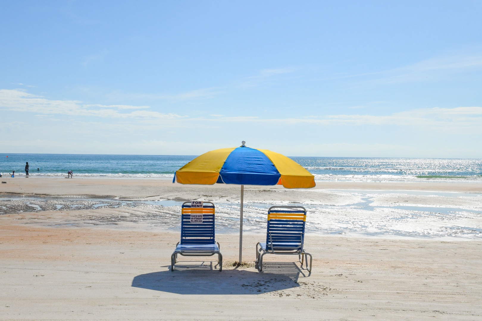 Sandy beach with ocean waves, shaded lounge chairs, and gentle surf under a bright sunny sky—perfect for a relaxing coastal escape.
