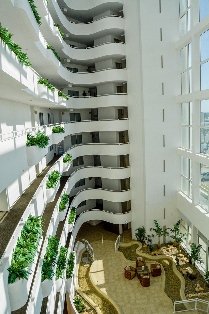 Step into a stunning multi-story atrium where curved balconies and tropical plants create your own private resort experience.