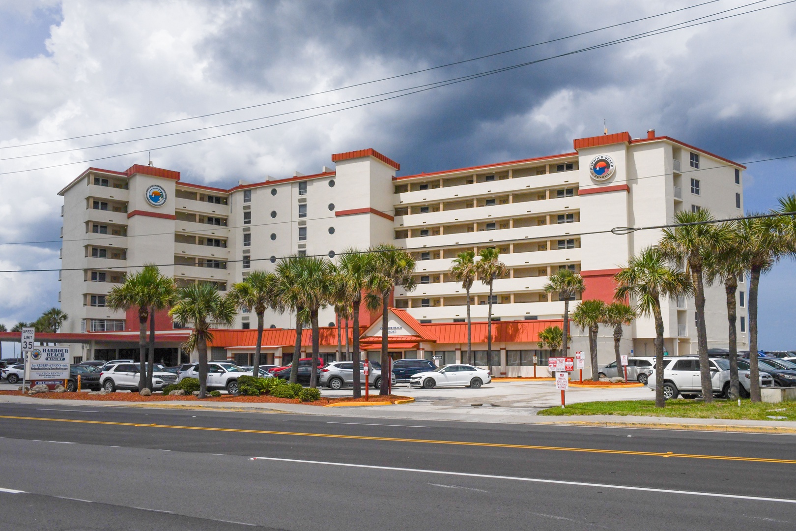 A beachfront vacation rental building featuring balconies and palm trees, located along a main thoroughfare near the coast.
