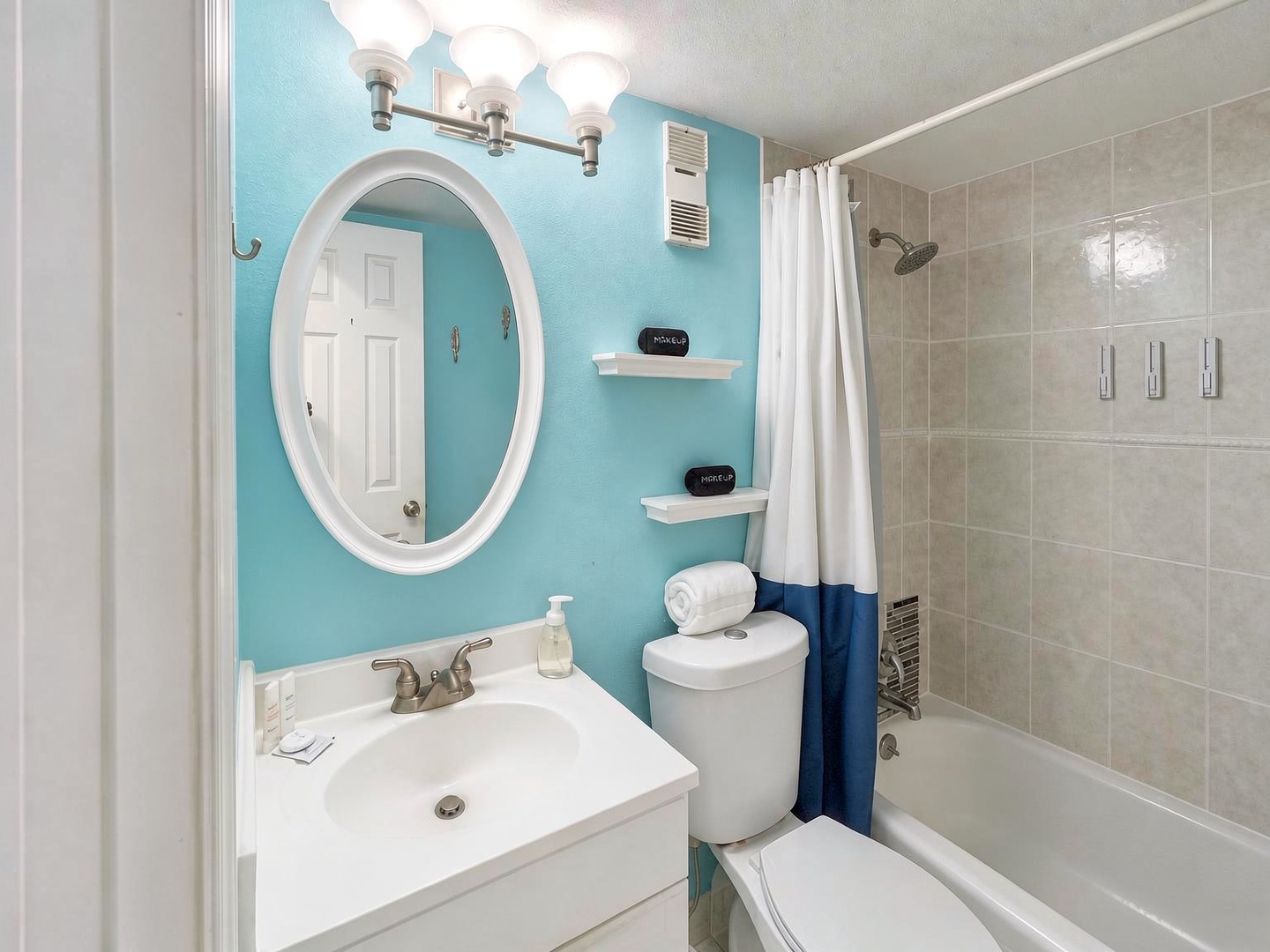 Step into your private bathroom where calming turquoise walls meet crisp white fixtures. Fresh towels await, and your shower features modern tile work and thoughtful storage—everything you need to refresh and unwind.