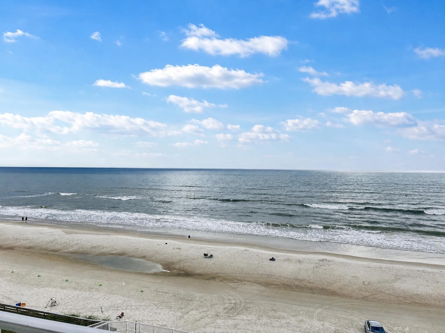 A wide stretch of pristine sand meets gentle rolling waves under an expansive sky. The beach is part of the surrounding area near the property.