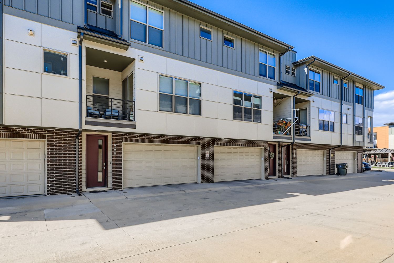 Modern townhome community featuring contemporary architecture with clean lines, mixed materials of brick and siding, private balconies, and attached two-car garages for convenient arrival and parking.