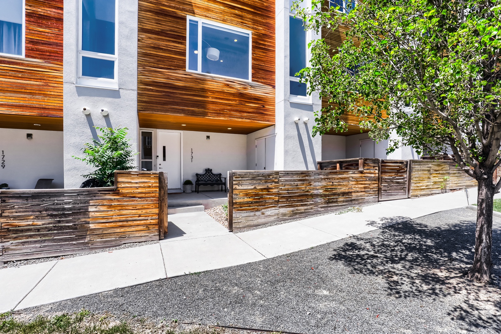Modern townhome featuring warm wood siding, stylish horizontal-slat fencing, and covered parking—an inviting arrival on a quiet, tree-lined street.